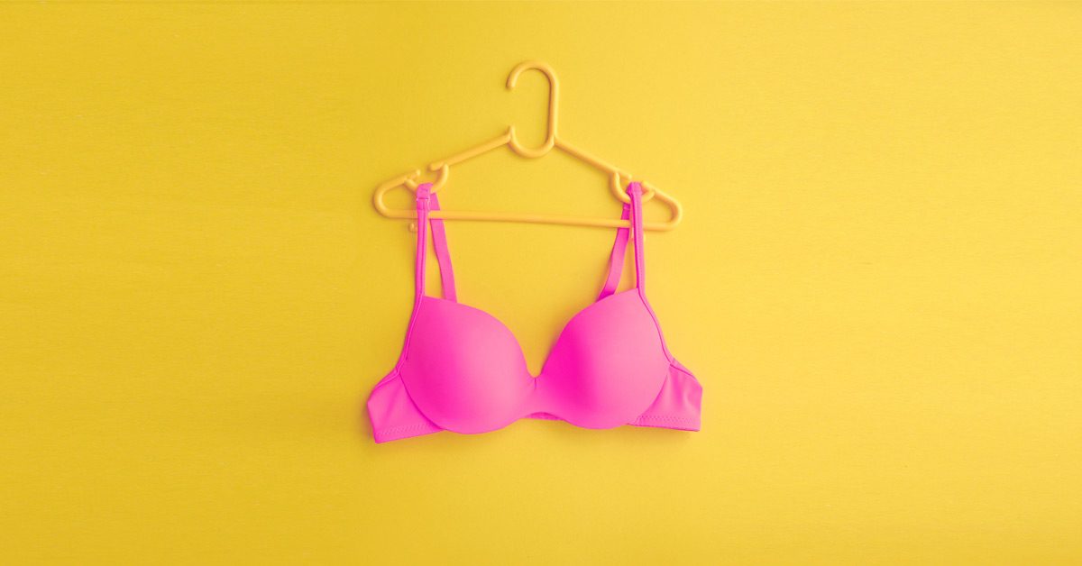 Pink bra hanging on a yellow backdrop - bra shopping after breast augmentation