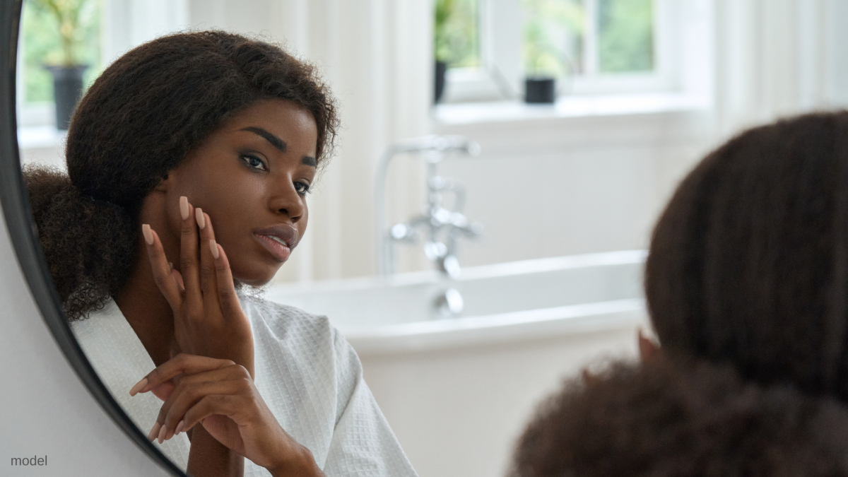 Woman looking in the mirror touching face (MODEL)