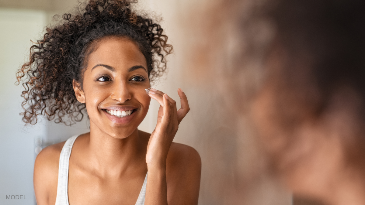 Woman smiling in a mirror and touching face with hand. (MODEL)